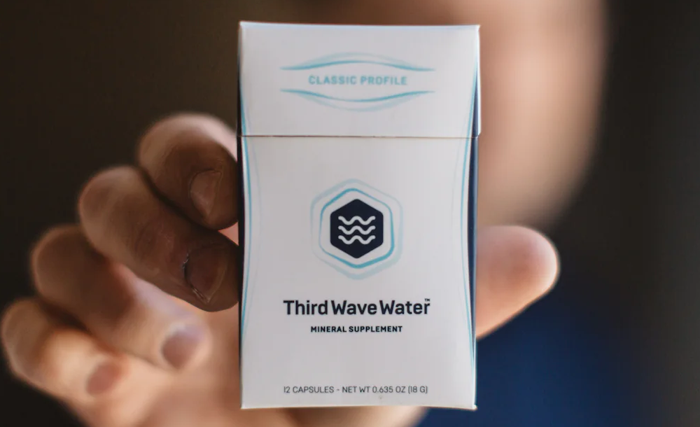 Hand holding a package of Third Wave Water mineral supplement.