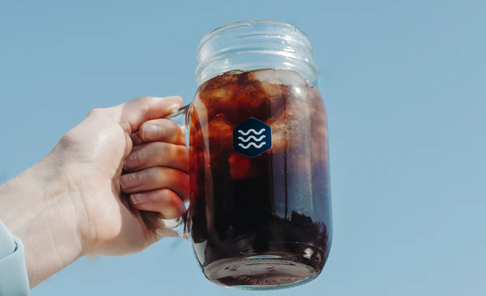 Hand holding iced coffee against a clear blue sky