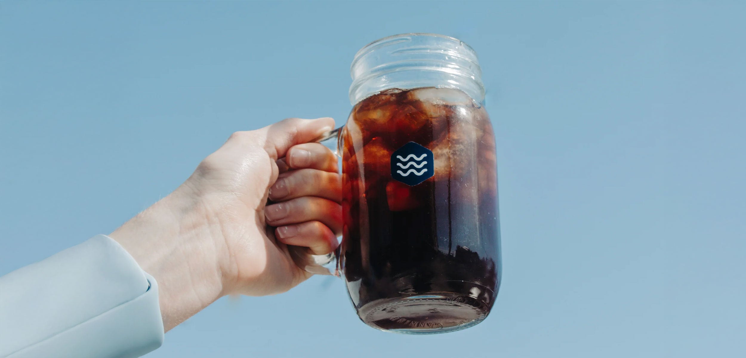 Hand holding iced coffee against a clear blue sky